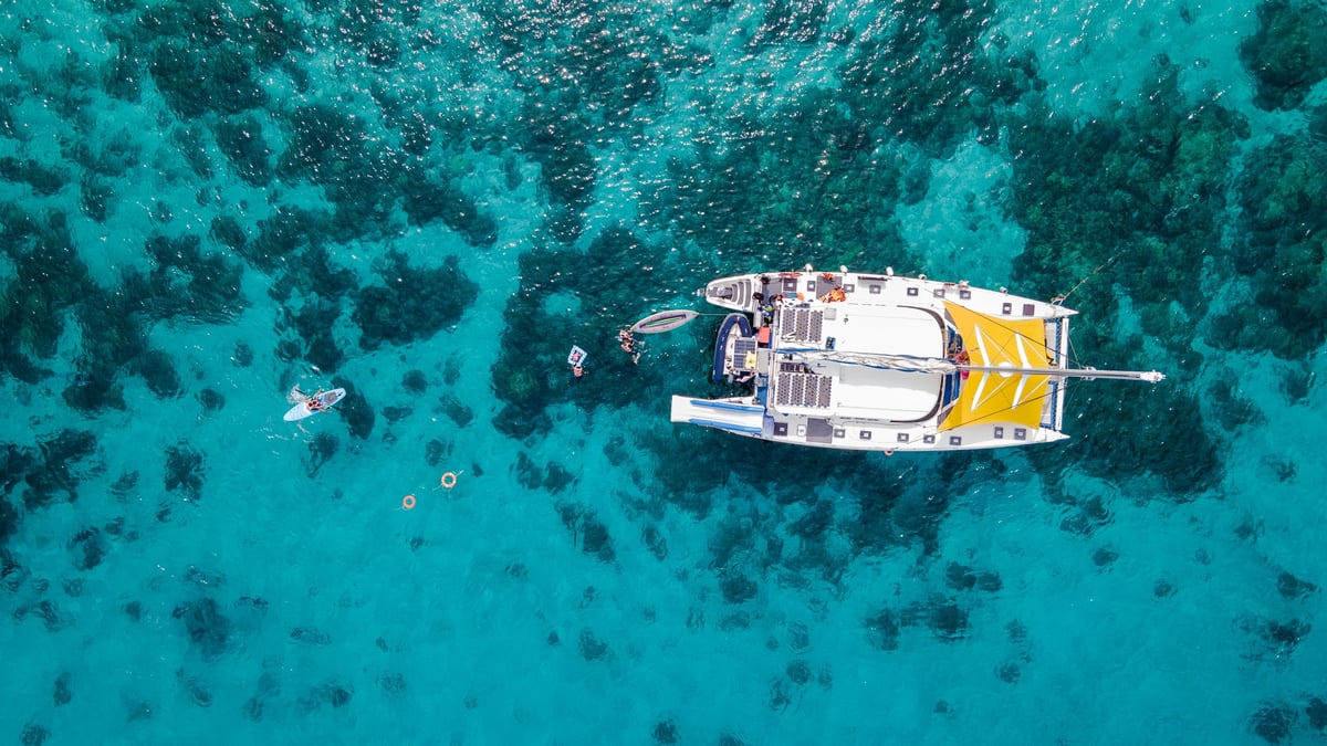 Aerial top view of sailing catamaran over turquoise water with tourists swimming