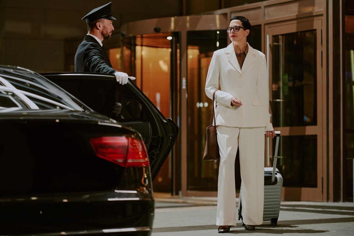 Black man chauffeur in uniform opening car door at hotel entrance, premium Caribbean transportation service