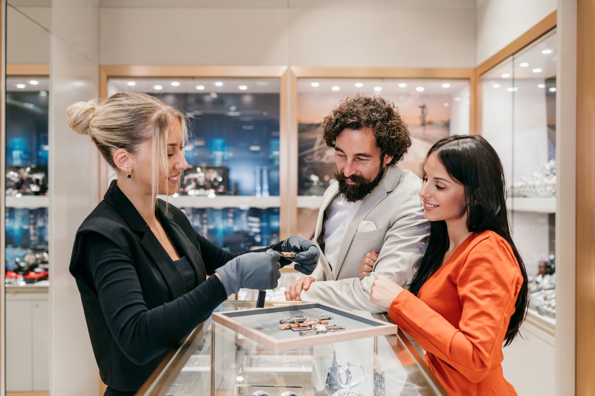 Saleswoman presenting an elegant watch to a smiling couple in a luxury jewelry boutique