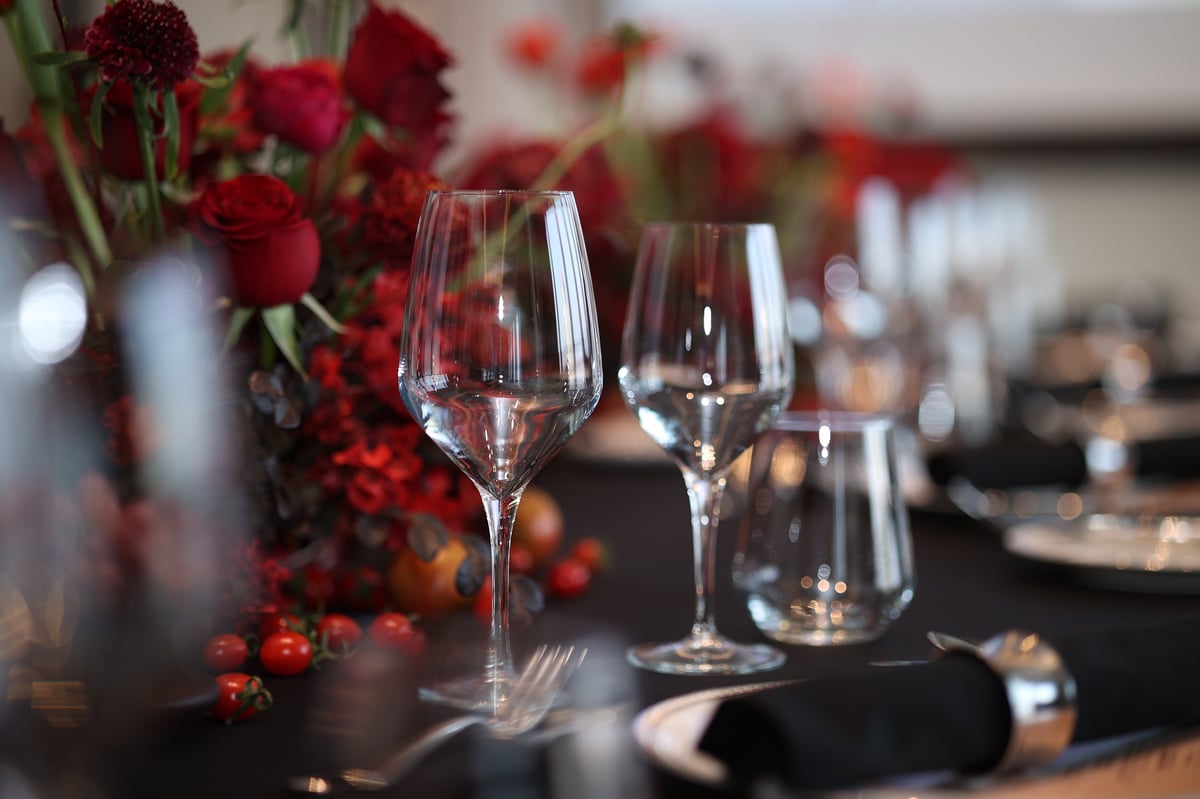 Upscale dining table with clear wine glasses, black napkins, shiny cutlery, and red floral centerpiece creating a luxurious atmosphere