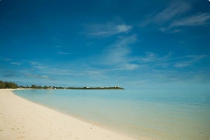Pristine sandy beach with turquoise water and small island visible on the horizon under a clear blue sky