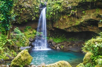 Waterfall cascading into turquoise pool surrounded by lush green moss-covered rocks and jungle foliage