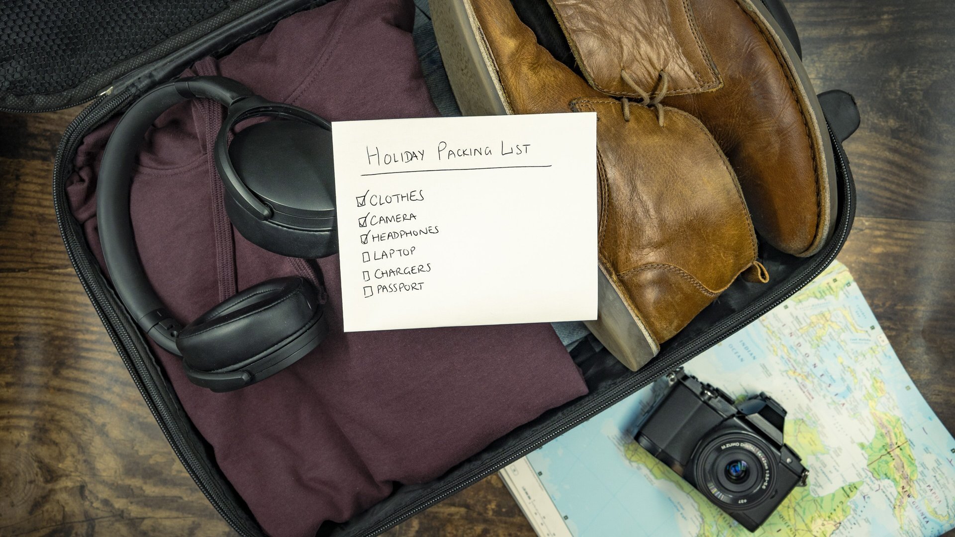 Open suitcase with clothes, shoes, headphones, a camera, a map and a handwritten holiday packing list