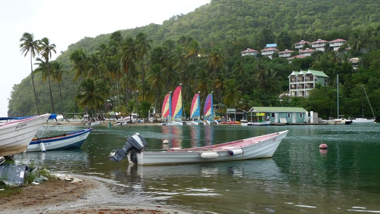 Small boats and colorful sailboards on the calm water of Marigot Bay, St. Lucia, with palm-covered hills behind