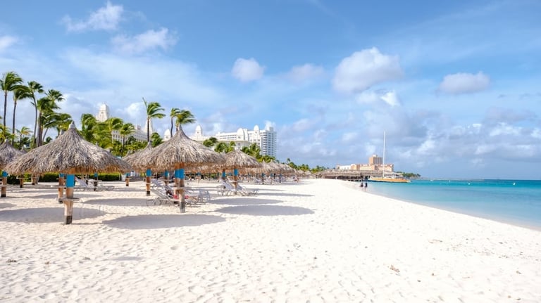 Tropical beach with white sand, palm trees, thatched umbrellas, and turquoise water under blue sky