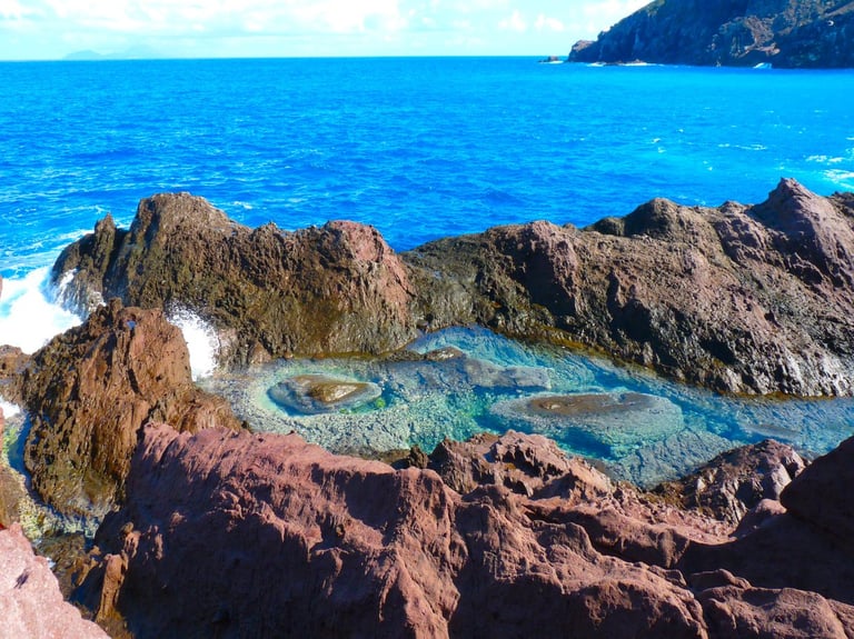 Turquoise tidal pool surrounded by rocky volcanic formations with deep blue ocean and cliffs in background