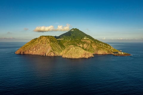 Small volcanic island with green vegetation surrounded by blue ocean under clear sky
