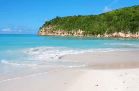 Tropical beach with white sand, turquoise water, and lush green cliffs under blue sky
