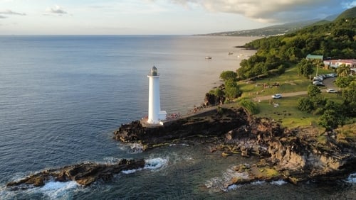 White lighthouse on rocky headland surrounded by ocean and green coastal landscape