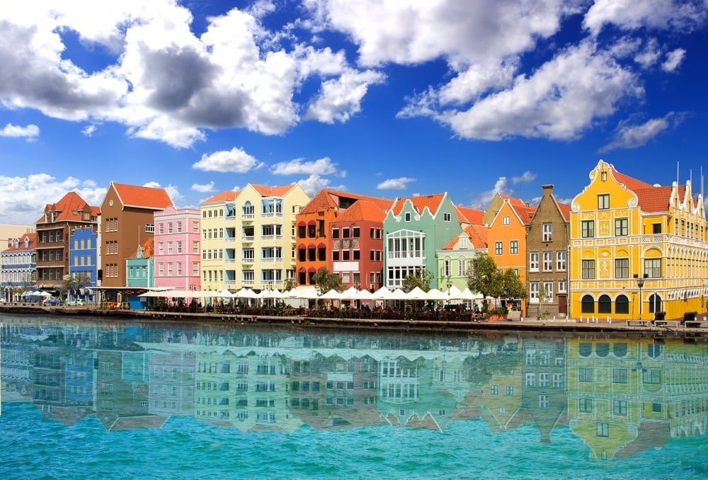 Colorful waterfront buildings reflected in turquoise water under blue sky with white clouds