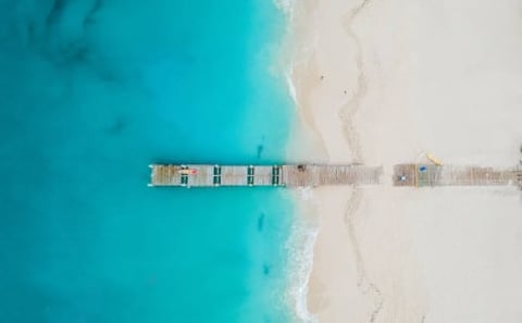 Aerial view of wooden pier extending into turquoise ocean water with white sandy beach