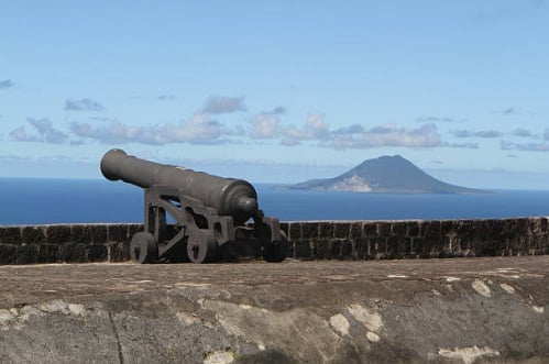 Historic cannon mounted on stone fortification wall overlooking ocean with distant volcanic island