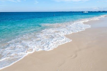 Tropical beach with turquoise waves rolling onto white sand, distant boats on blue ocean horizon