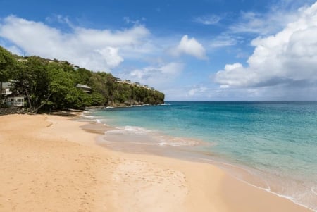 Tropical beach with sandy shore, turquoise water, lush green vegetation, and blue sky with white clouds