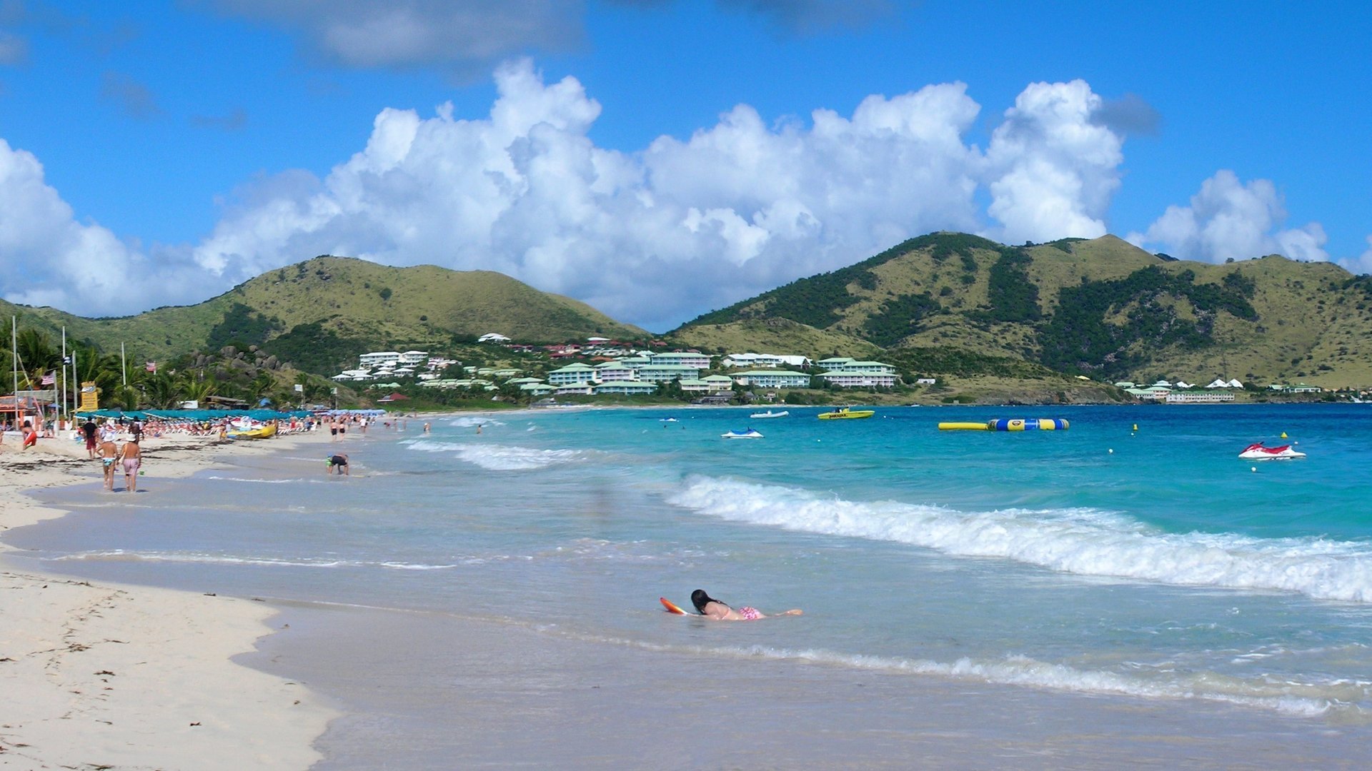 White sand and turquoise surf along Orient Bay (Baie Orientale), with green hills behind, on the French side of St. Martin