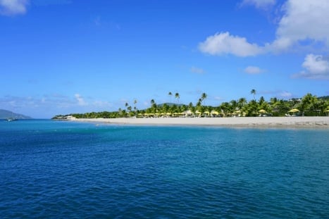 Tropical beach with turquoise water, white sand, and palm trees under a blue sky