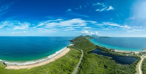 Aerial view of a green peninsula with sandy beach, blue ocean, and lagoon under clear sky