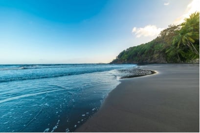 Serene black sand beach with turquoise ocean waters and lush green jungle vegetation under blue sky