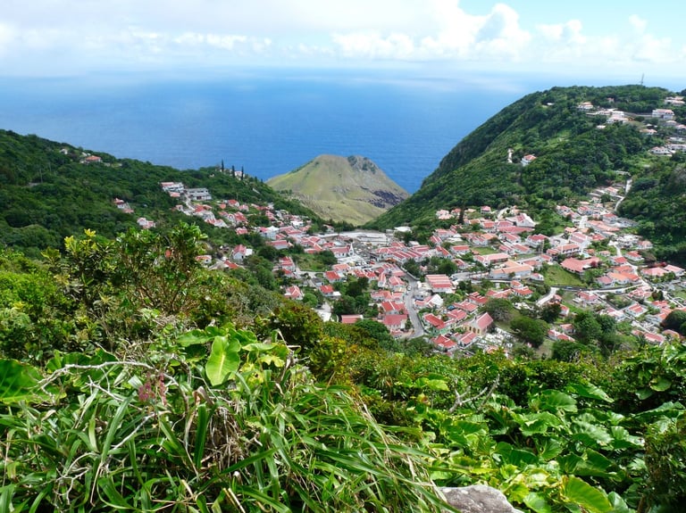 Aerial view of a coastal village nestled in lush green hills overlooking blue ocean waters