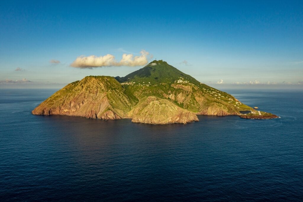 Lush volcanic island with green peaks surrounded by calm blue ocean water under clear sky