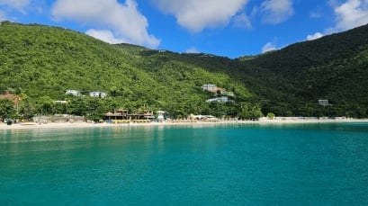 Tropical beach resort nestled between lush green hills with turquoise water and white sandy beach under blue sky