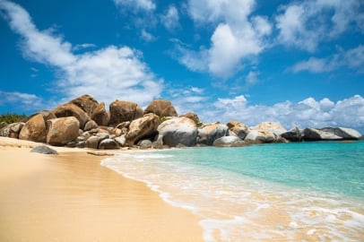 Sandy beach with turquoise water and large boulders under a blue sky with white clouds