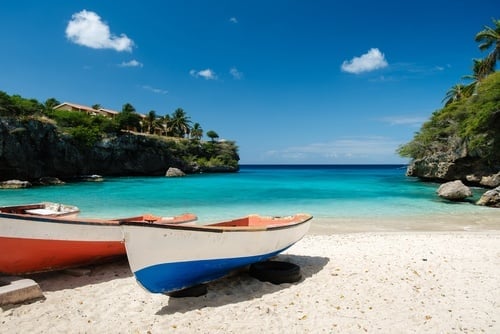 Colorful fishing boats on sandy beach with turquoise water and tropical vegetation under blue sky