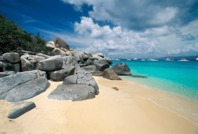 Tropical beach with pristine turquoise water, white sand, and large granite boulders under blue sky with clouds
